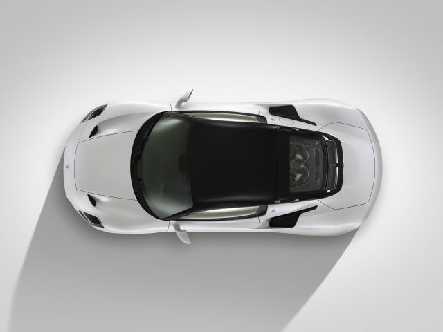 Bovenaanzicht van een witte Maserati MC20 met een zwart dak en getinte ramen op een grijze achtergrond.