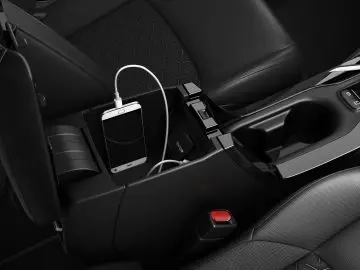 Binnenaanzicht van een Suzuki Swace met een smartphone die wordt opgeladen in de middenconsole, met aangesloten kabels en stoelen op de achtergrond.