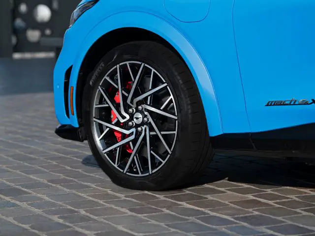 Close-up van de lichtmetalen velg van een blauwe auto met rode remklauwen, waarop de modelnaam 