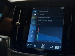 Aanraakscherm op de middenconsole in een Volvo-auto met navigatie, telefoonconnectiviteit en luchtkwaliteitsindex, terwijl de wijzers de instellingen aanpassen.