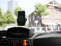 Smartphone gemonteerd op het dashboard van een auto en toont de AutoModus-app, met een wazig gebouw op de achtergrond.