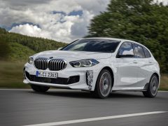 Een witte BMW 128ti rijdend op een snelweg onder een bewolkte hemel.