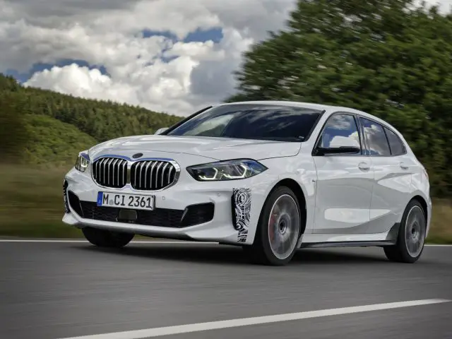 Een witte BMW 128ti rijdend op een snelweg onder een bewolkte hemel.