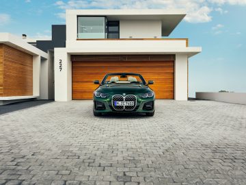 Een groene BMW 4 Serie Cabrio geparkeerd voor een modern huis van twee verdiepingen met een grote houten garagedeur.