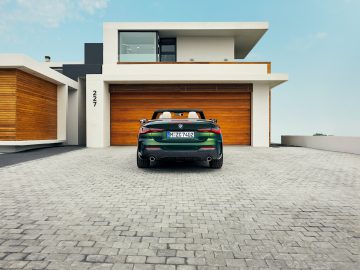 Een BMW 4 Serie Cabrio geparkeerd voor een modern huis met een houten garagedeur en adresnummer 247 op een zonnige dag.