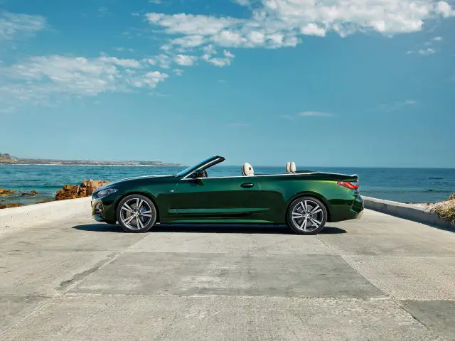 Een groene BMW 4 Serie Cabrio geparkeerd op een kustweg, met helderblauwe lucht en rotsachtige kust op de achtergrond.
