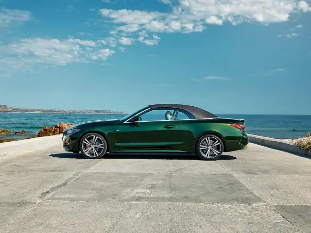 Een groene BMW 4 Serie Cabrio geparkeerd op een kustweg met de oceaan en de rotsachtige kust op de achtergrond onder een helderblauwe lucht.