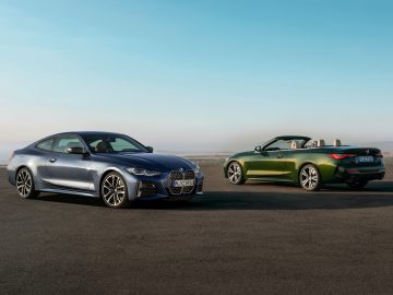 Twee BMW-auto's, een grijze coupé en een groene 4 Serie Cabrio, staan geparkeerd op een vlak open terrein met een wazige lucht op de achtergrond.