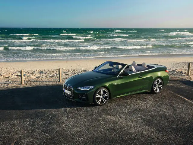 Een groene BMW 4 Serie Cabrio geparkeerd aan de kust met een houten hek, onder een heldere hemel en een turbulente oceaan op de achtergrond.