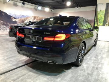 Een blauwe BMW 5 Serie geparkeerd op een binnententoonstelling met een achtergrond met bergthema.