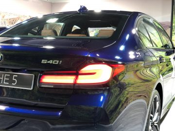 Achteraanzicht van een blauwe BMW 5 Serie-auto met de achterlichten aan, binnen geparkeerd en een glanzende afwerking reflecterend.