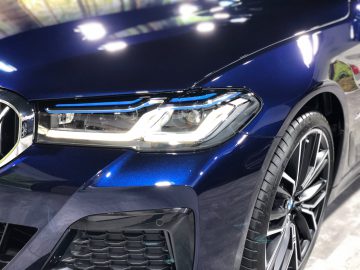Close-up van de voorkant van een blauwe BMW 5 Serie, waarbij de nadruk ligt op de strakke LED-koplampen en het gedetailleerde grille-ontwerp.
