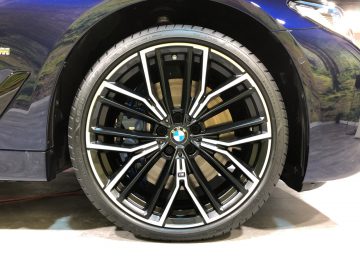 Close-up van een lichtmetalen velg van een BMW 5 Serie-auto met een blauw-wit logo in het midden, tentoongesteld op een tentoonstelling.