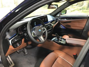 Binnenaanzicht van een auto uit de BMW 5-serie met het stuur, het dashboard en de leren stoelen.