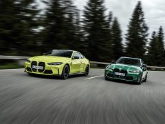 Twee BMW M3 Sedan-auto's, een limoengroene en een donkergroene, racen op een bochtige bosweg.