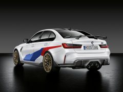 Achteraanzicht van een witte BMW M3 Sedan met een blauwe en rode streep, geparkeerd in een studio met een grijze achtergrond.