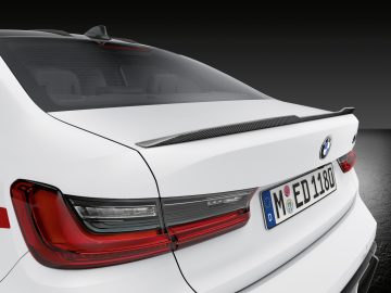 Achteraanzicht van een witte BMW M3 Sedan met achterlichten, kofferbak en logo met een Europees kenteken, op een donkere achtergrond.