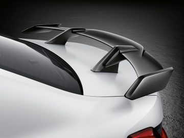 Close-up van de achterkant van een witte BMW M3 Sedan met een koolstofvezelspoiler, van bovenaf gezien op een donkere achtergrond.