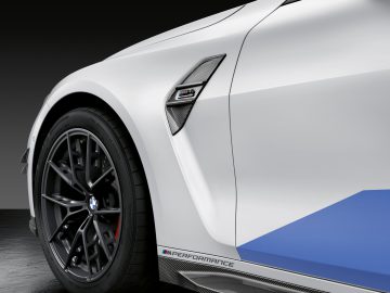 Close-up van een witte BMW M3 Sedan-sportwagen, gericht op het voorwiel en het zijpaneel met prestatielogo.