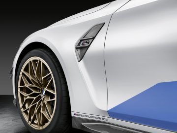 Close-up van de voorkant en het stuur van een witte BMW M3 Sedan, met een strak ontwerp en prestatiebadge.