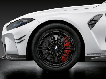 Close-up van een witte BMW M3 Sedan, gefocust op het voorwiel, met zwarte lichtmetalen velgen en rode remklauwen.