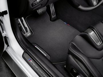 Binnenaanzicht van een BMW M3 Sedan met een deur, stoel met lederen bekleding en vloerbedekking met een logo, met de nadruk op luxueus design en materialen.