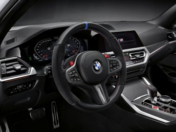 Binnenaanzicht van een BMW M3 Sedan met het stuur, het dashboard en de middenconsole met digitale displays en bedieningselementen.