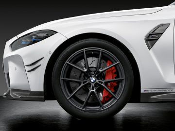 Close-up van het voorwiel van een witte BMW M3 Sedan met zichtbare M Performance-markeringen en rode remklauwen.