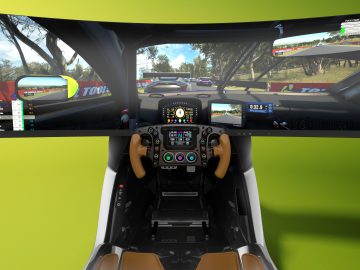 First-person-aanzicht vanuit een Aston Martin-raceautosimulator met een gedetailleerd dashboard en meerdere schermen met een virtueel racespel.
