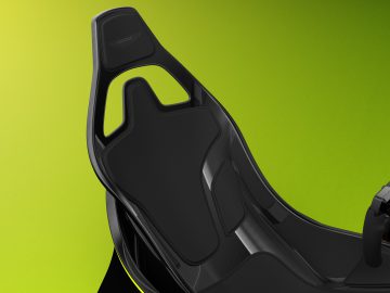 Zwart Aston Martin raceautostoeltje op een groene achtergrond, met gedetailleerde stiksels en ergonomisch ontwerp.