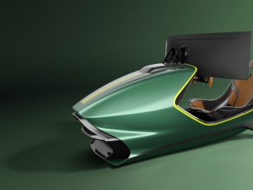 Futuristische Aston Martin racesimulatoropstelling met een strakke groene behuizing, geïntegreerde monitor en een enkele oranje stoel op een donkergroene achtergrond.
