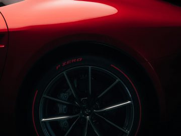 Close-up van de achterkant en het wiel van een rode Ferrari Omologata met een Pirelli P Zero-band, tegen een donkere achtergrond.