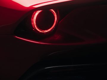 Close-up van het achterlicht en de ontwerpdetails aan de achterkant van een Ferrari Omologata in een donkere omgeving, waarbij het ronde licht en de uitlaatpijpen benadrukt worden.