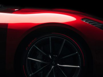 Zijaanzicht van de rode Ferrari Omologata-sportwagen, gericht op het ronde spatbord en wiel met zichtbare 'r spec'-bandmarkering, tegen een donkere achtergrond.