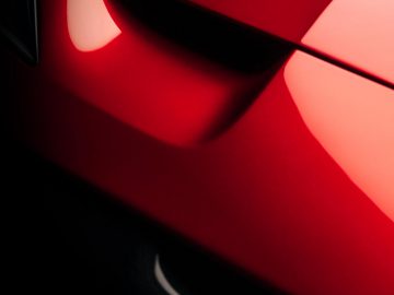 Close-up van een rode Ferrari Omologata, gericht op strakke designlijnen en de abstracte weerkaatsing van licht op het oppervlak.