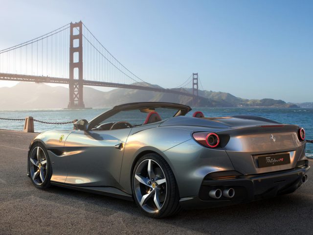 Een zilveren Ferrari Portofino M geparkeerd aan de kust met de Golden Gate Bridge op de achtergrond op een heldere dag.