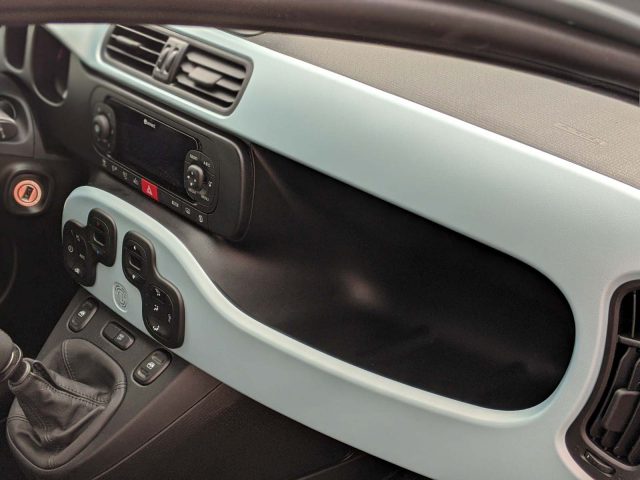 Interieur van een Fiat Panda met het dashboard, de versnellingspook en de bestuurdersdeur met bedieningselementen voor ramen en spiegels.