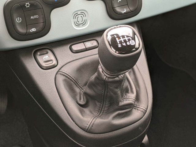 Handmatige versnellingspook en bedieningselementen in een Fiat Panda, met zwart lederen kofferbak en gedetailleerde knop met de versnellingsnummers.