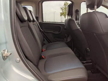 Binnenaanzicht van een Fiat Panda met de achterbank en de binnenkant van de open linker achterdeur, met de nadruk op de schone, donkere bekleding.