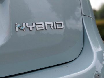 Close-up van een hybride Fiat Panda-embleem op de achterkant van een grijze auto, met de nadruk op het woord 'hybride' in zilveren letters.
