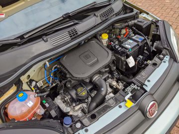Open autokap met een gedetailleerd aanzicht van de motorruimte van een Fiat Panda met zichtbare componenten, waaronder de accu, het luchtfilter en het koelvloeistofreservoir.