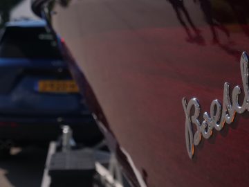 Close-up van een glanzende 'rebellen'-badge op een rode Ford Explorer PHEV met een andere blauwe auto wazig op de achtergrond.