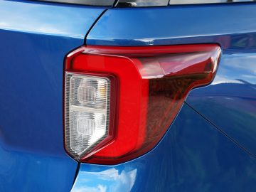 Close-up van een rood achterlicht op een blauwe Ford Explorer PHEV, met gedetailleerd ontwerp en reflectie op glanzend oppervlak.