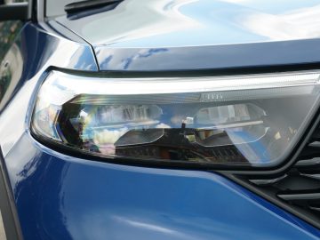 Close-up van de koplampunit van een Ford Explorer PHEV, met gedetailleerde ontwerpelementen en reflecties op het oppervlak.