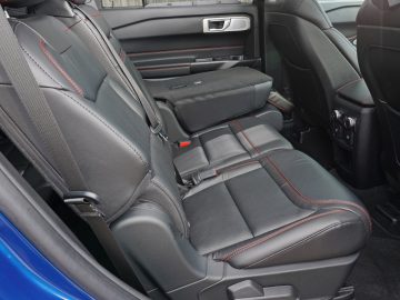 Interieur van een Ford Explorer PHEV met zwartleren achterbank met rode stiksels, armleuning omlaag en klimaatregeling.