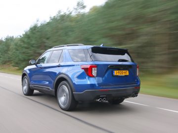 Een blauwe Ford Explorer PHEV SUV die op een snelweg rijdt met bewegingsonscherpte op de achtergrond, wat de snelheid benadrukt.