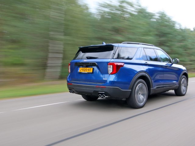 Een blauwe Ford Explorer PHEV die met hoge snelheid over een snelweg rijdt en bewegingsonscherpte op de achtergrond vertoont.