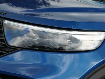 Close-up van de koplamp van een blauwe Ford Explorer PHEV en een deel van de grille.