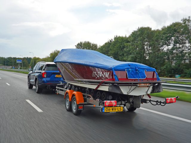 Een Ford Explorer PHEV die een overdekte boot op een dubbelassige aanhanger over een snelweg sleept.