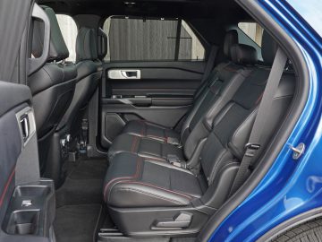 Binnenaanzicht van een Ford Explorer PHEV met zwartleren stoelen met rode stiksels en een gedeeltelijk geopende deur.